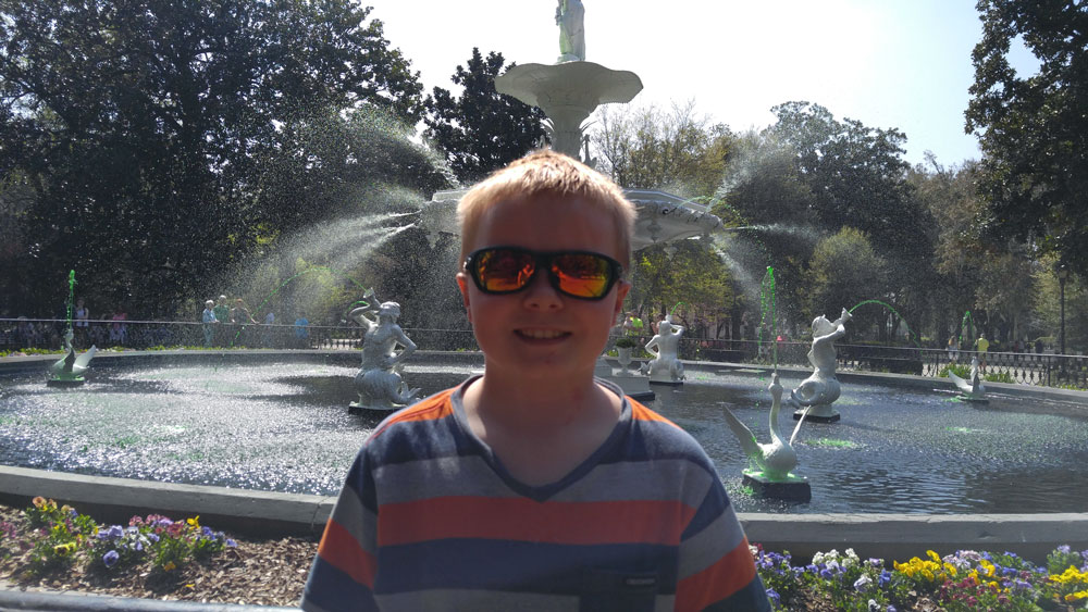 A young boy standing in front of the fountain at Forsyth Park.