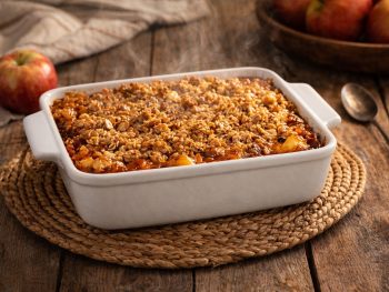 Freshly baked apple crisp in a white ceramic 9x9 baking dish with golden oat crumb topping and bubbling apple filling on a rustic farmhouse table