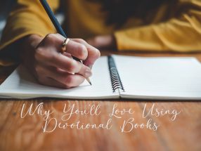 A close-up of a person writing in a devotional journal with a pen, wearing a gold ring and mustard-colored sweater, symbolizing reflection and daily scripture study.